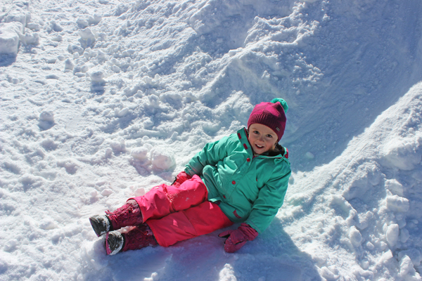 little girl plays on snow mound