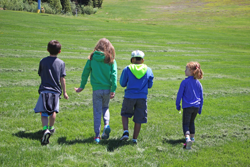 four kids walk on grass